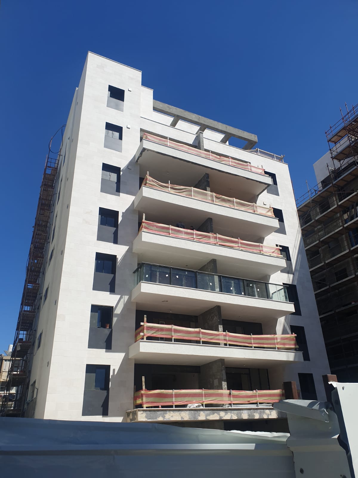 חזית בניין מגורים עם חיפוי אבן ומרפסות בשלבי גמר
